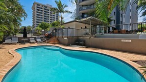 Piscina com borda azulejada, rodeada por espreguiçadeiras e uma pequena área de deck.