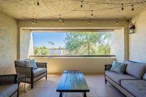 Relax on the balcony with a clear view of the surrounding greenery and buildings, surrounded by a black table and two sofas with patterned cushions.