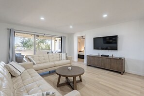 A modern living room with a beige sectional sofa, a round coffee table, and a flat-screen TV on a wooden cabinet. - Elegant Old Town Condo with Heated  Pool & Hot Tub (Scottsdale)
