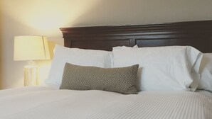 A neatly made bed with white linens and a patterned pillow, a wooden headboard, and a bedside lamp. - On TheRock BnB ~ Modern Suite (Comox)