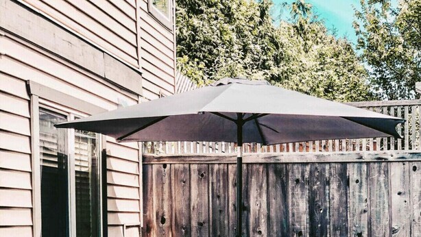 A patio with two turquoise chairs, a large umbrella, and potted plants. - On TheRock BnB ~ Modern Suite (Comox)