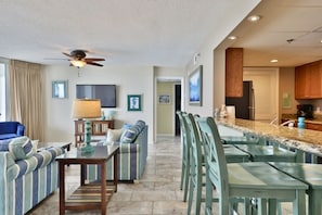A spacious living room with a sofa, a dining area with a bar, and a kitchen with wooden cabinets. - Newly Purchased 2BR 2BA @ THE LONG BEACH RESORT!!  4th floor Tower 1 (Panama City Beach)