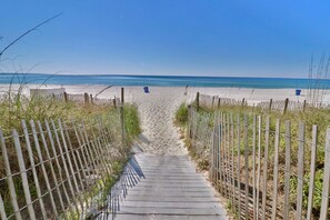 Un sentier en bois qui mène à une plage, avec un ciel dégagé.