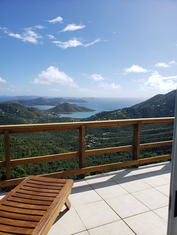 A wooden deck with a bench overlooking a mountainous landscape with a lake and distant hills. - Minutes from beaches & trails of the National Park, with a large bedroom . (St.John)