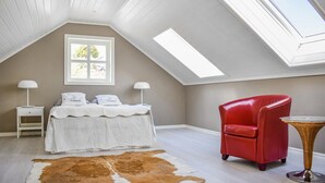 A bedroom with a sloped ceiling, a bed with white bedding, a red chair, a small table, and a cowhide rug.