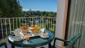 Un tavolo rotondo con prodotti per la colazione, vista su una piscina e ringhiera di un balcone.
