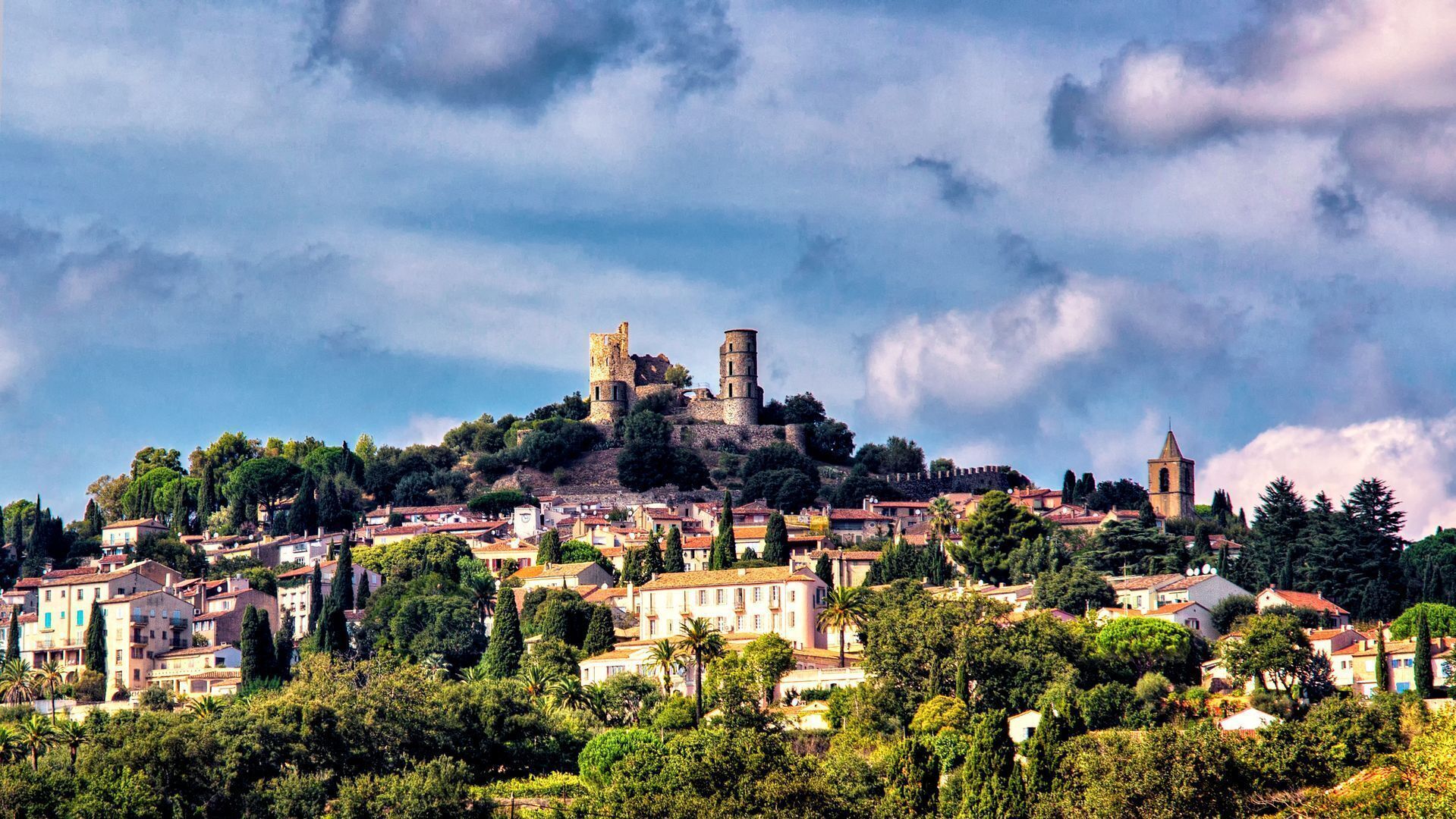 Un château historique, perché sur une colline, surplombe une ville où l’on trouve des bâtiments traditionnels et une végétation luxuriante.