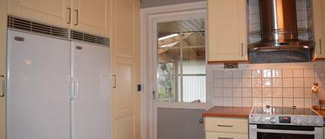 A kitchen with a refrigerator, oven, and a window.