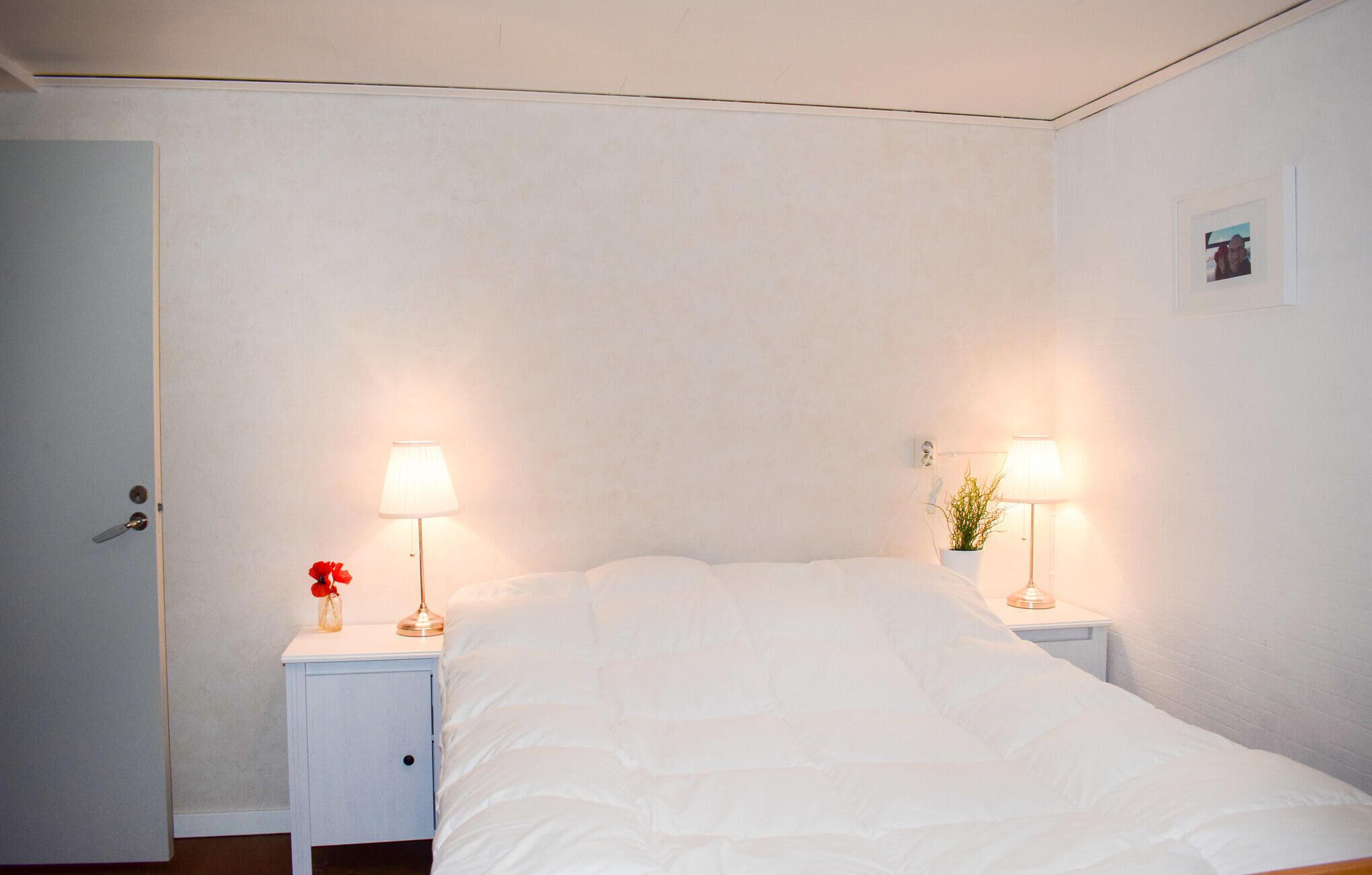A bedroom with a bed, two bedside tables with lamps, a door, and a small picture on the wall.