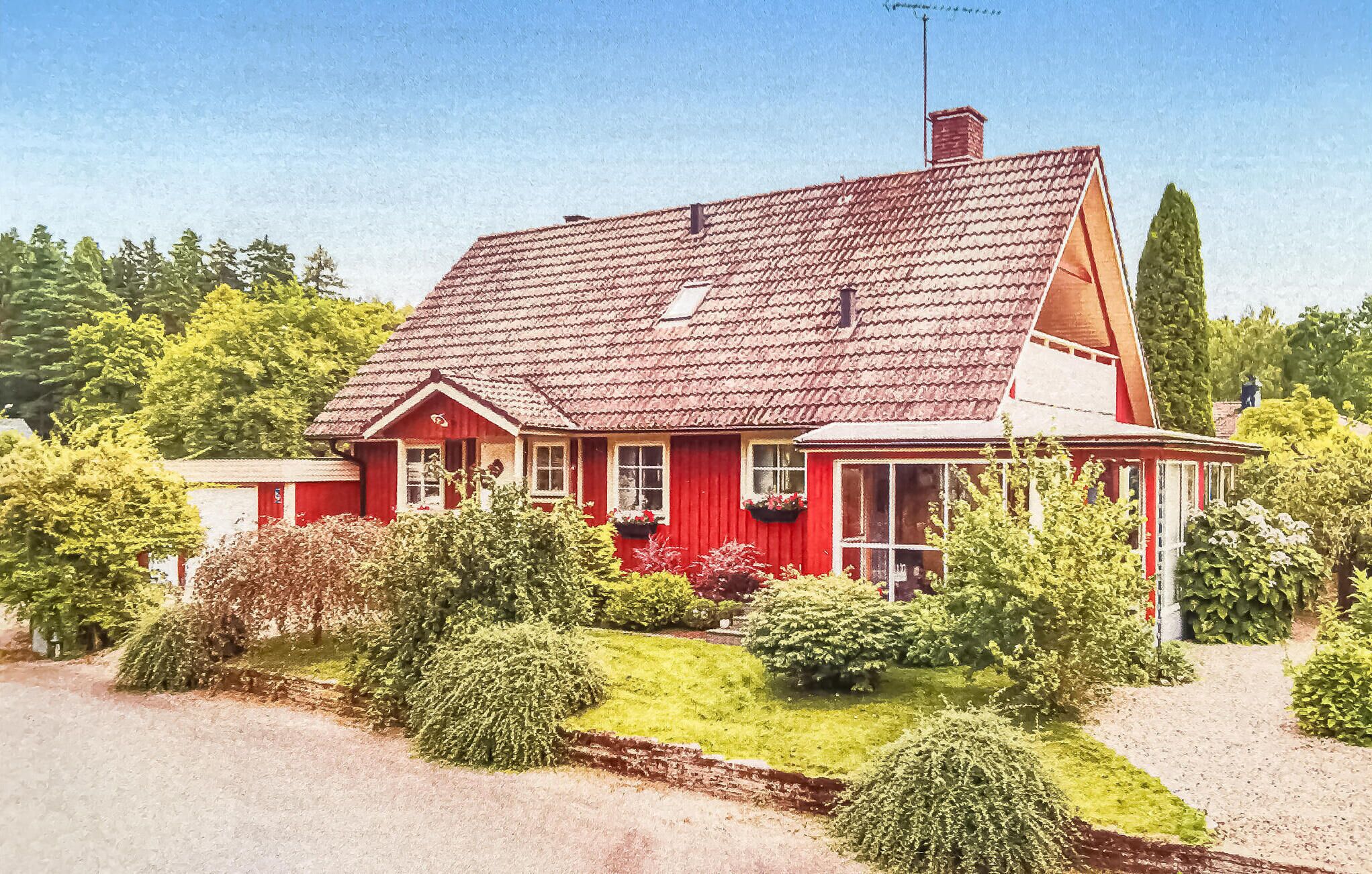 A red house with a sloped roof and a chimney, surrounded by well-maintained greenery and a clear sky.