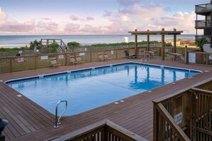 A swimming pool with a wooden deck, lounge chairs, and a view of the ocean. - Elevator. Oceanfront. Big Deck. Pool. (Carolina Beach)