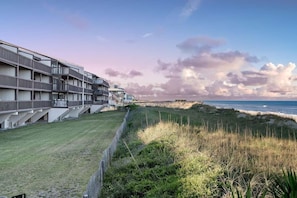 A coastal hotel with multiple balconies, a grassy lawn, and a view of the ocean. - Elevator. Oceanfront. Big Deck. Pool. (Carolina Beach)