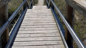Une promenade en bois qui mène à une plage, avec un ciel dégagé.