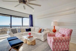 A modern living room with a white sofa, a patterned armchair, and a clear coffee table. - Elevator. Oceanfront. Big Deck. Pool. (Carolina Beach)