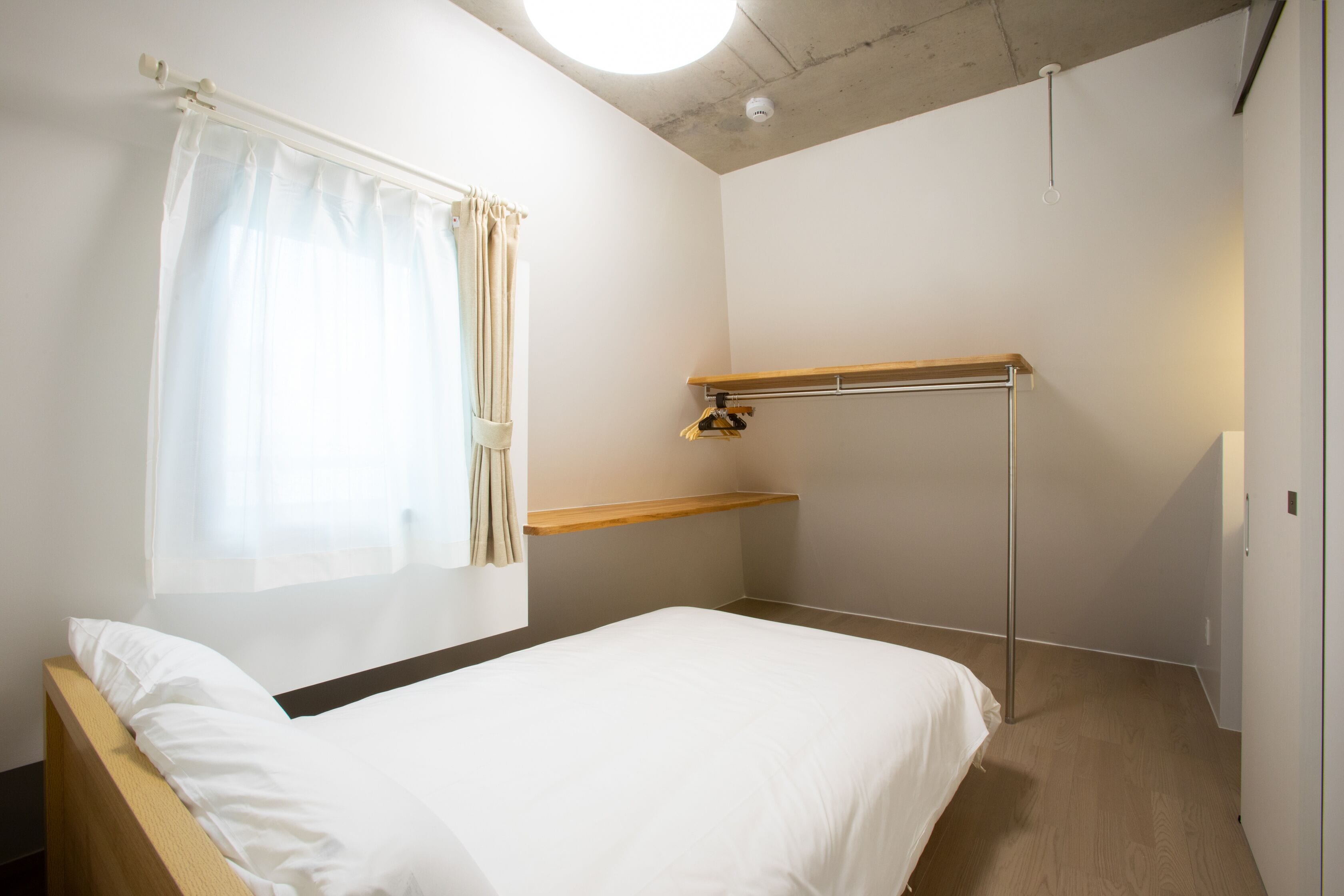 Un dormitorio con cama, ventana con cortinas, estante de madera y una lámpara en el techo.