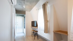 A modern, well-lit room with a wooden floor, a mounted TV, a small stool, and a window with curtains. - Laffitte Tokyo WEST (Tokyo)