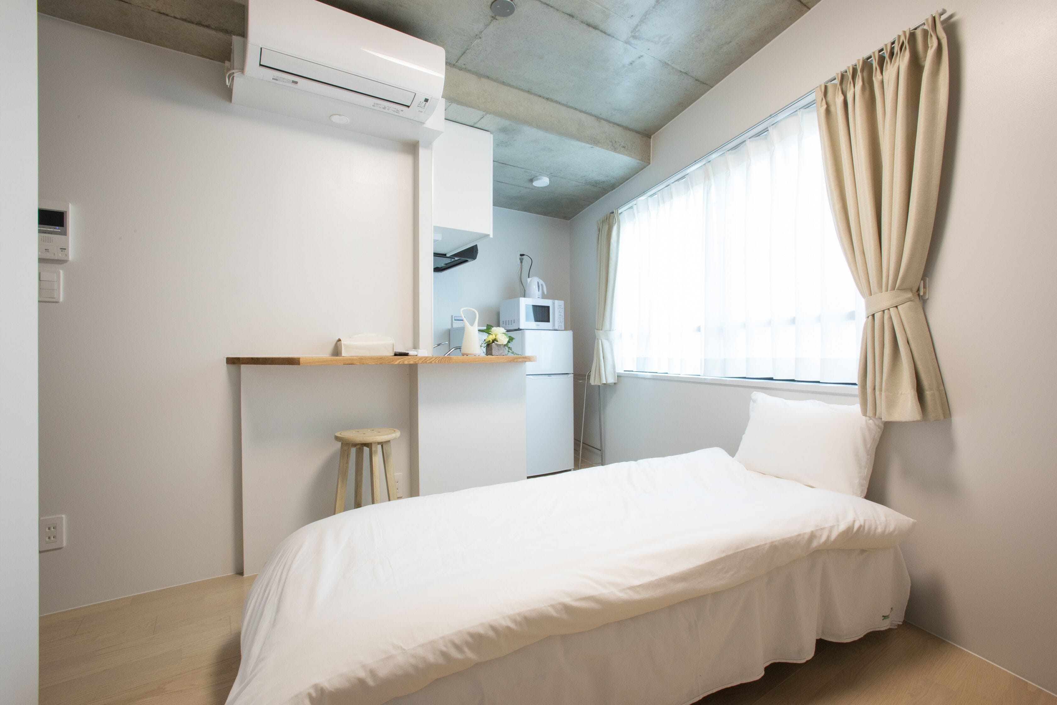 Habitació amb llit, una cuineta petita i finestra amb cortines.