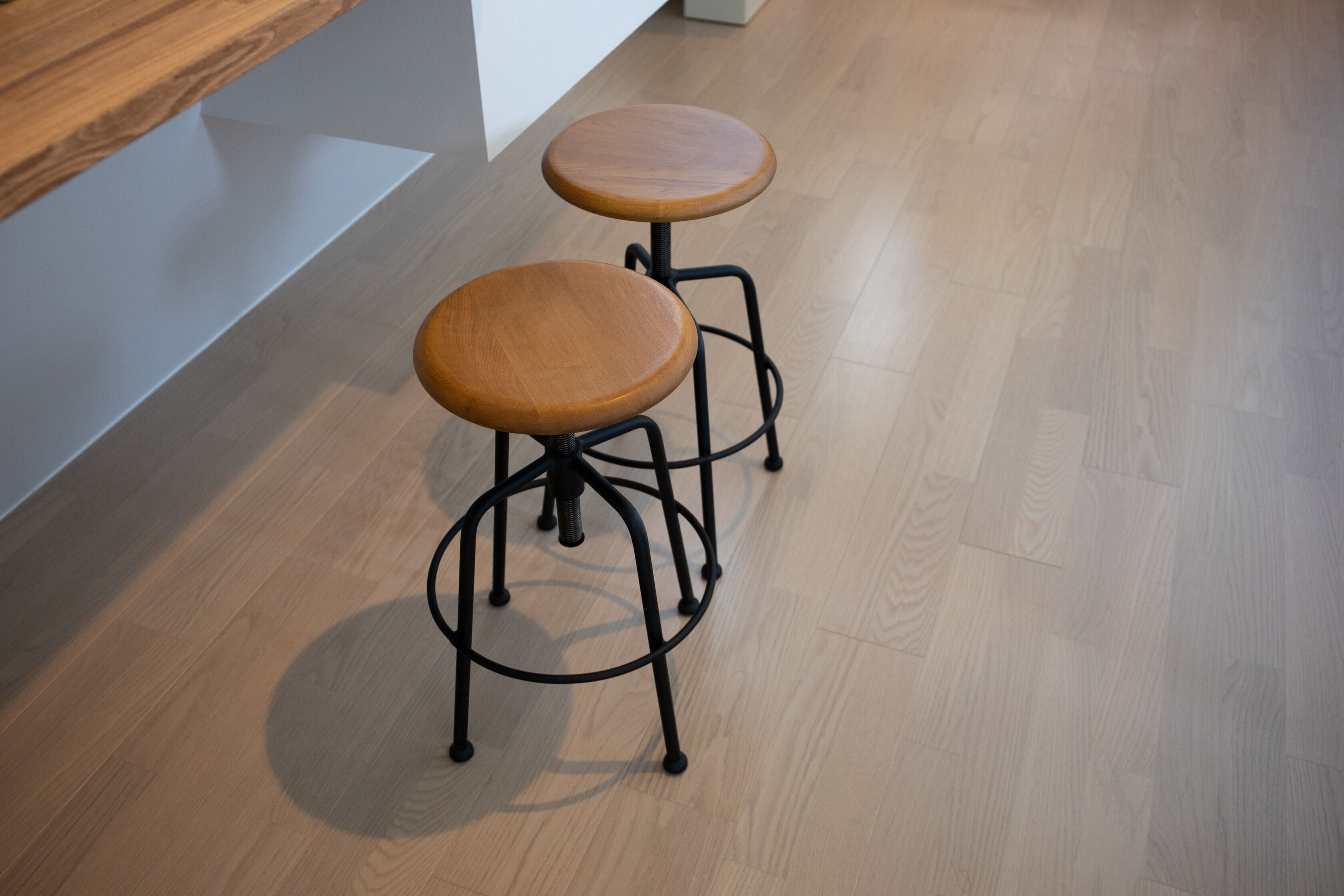 Deux tabourets en bois avec des pieds en métal, posés sur un plancher en bois.