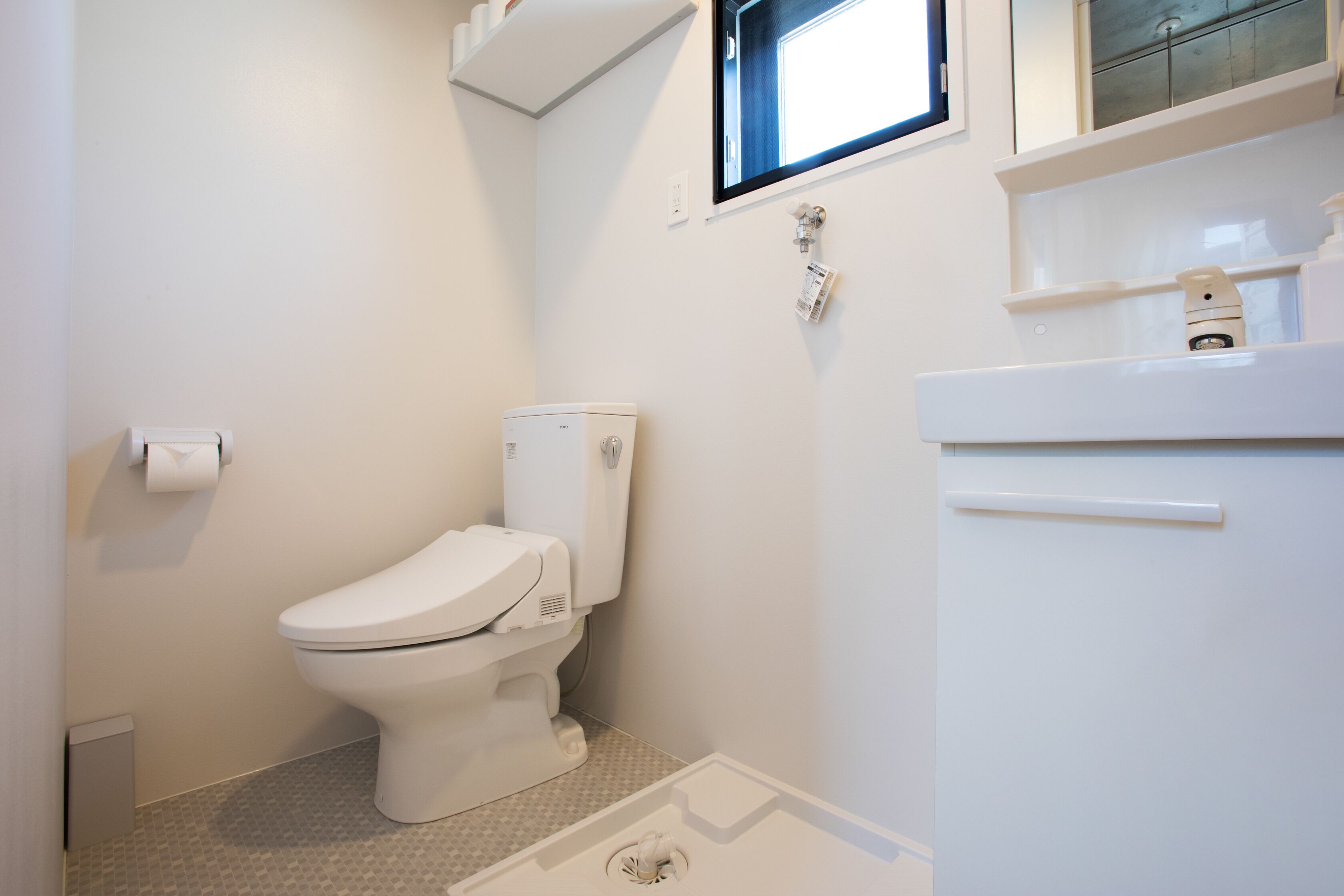 Un bany petit i net amb vàter, un lavabo i una finestra sobre el lavabo.