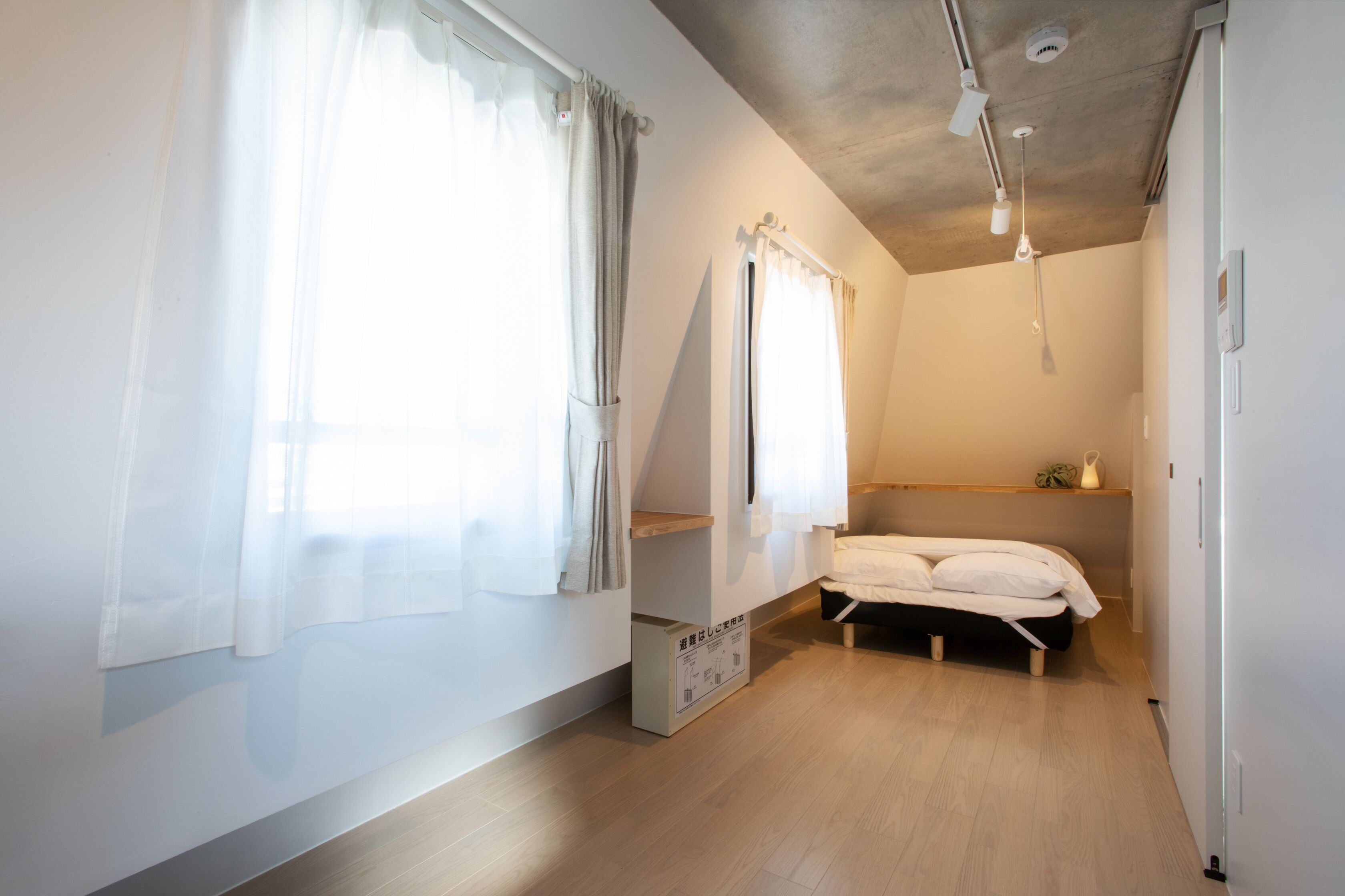A bedroom with a bed, a window with curtains, a shelf, and a ceiling light.
