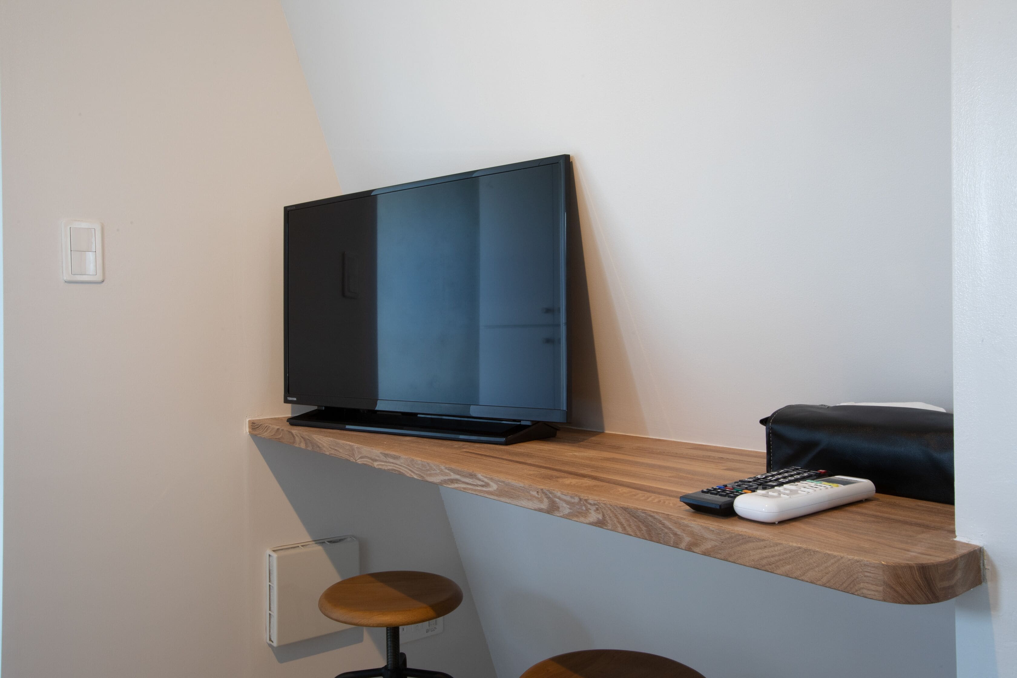 A flat-screen TV on a wooden shelf, a remote control, and a black bag.
