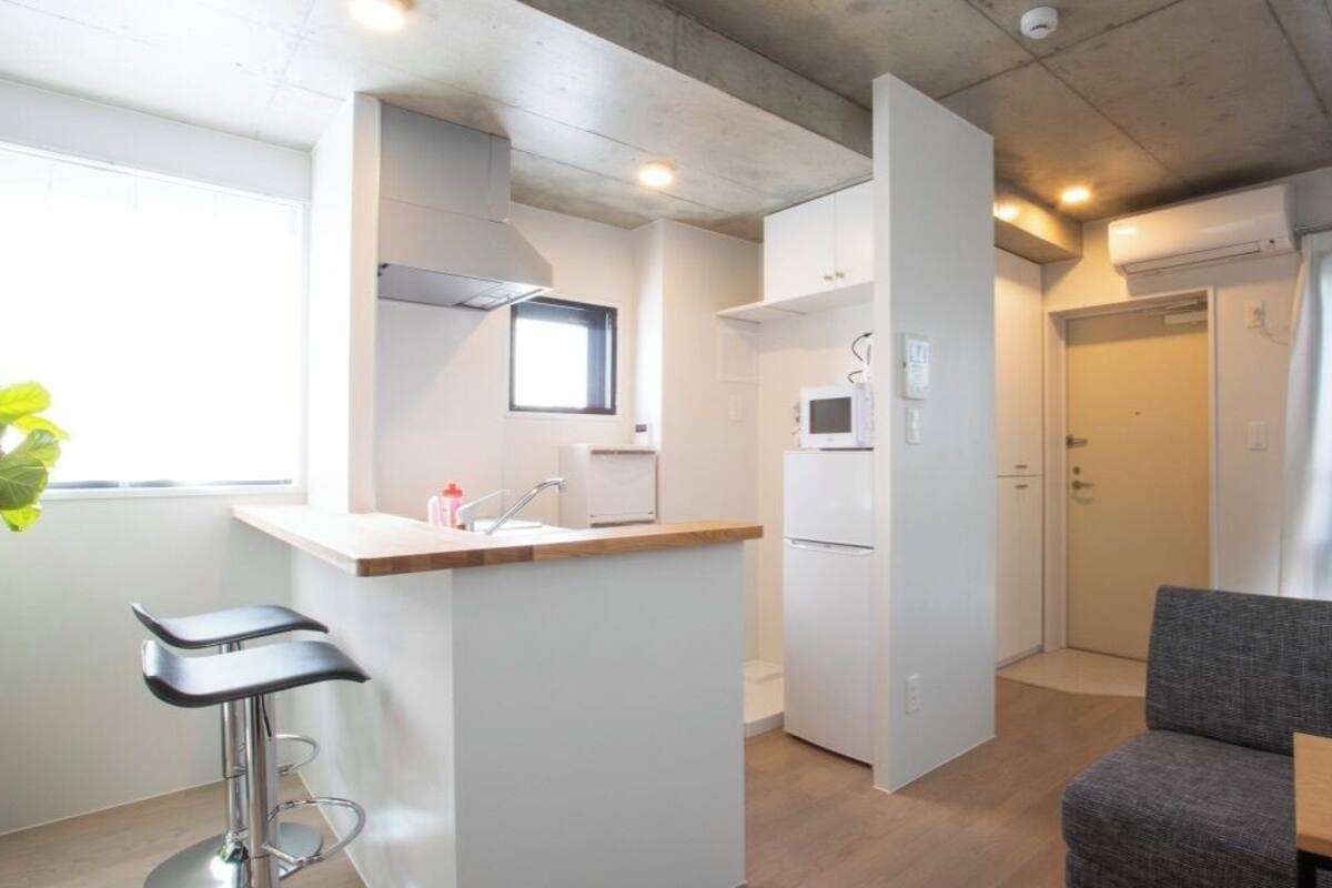 A compact living space with a kitchenette, a bar stool, a sofa, and a dining table.