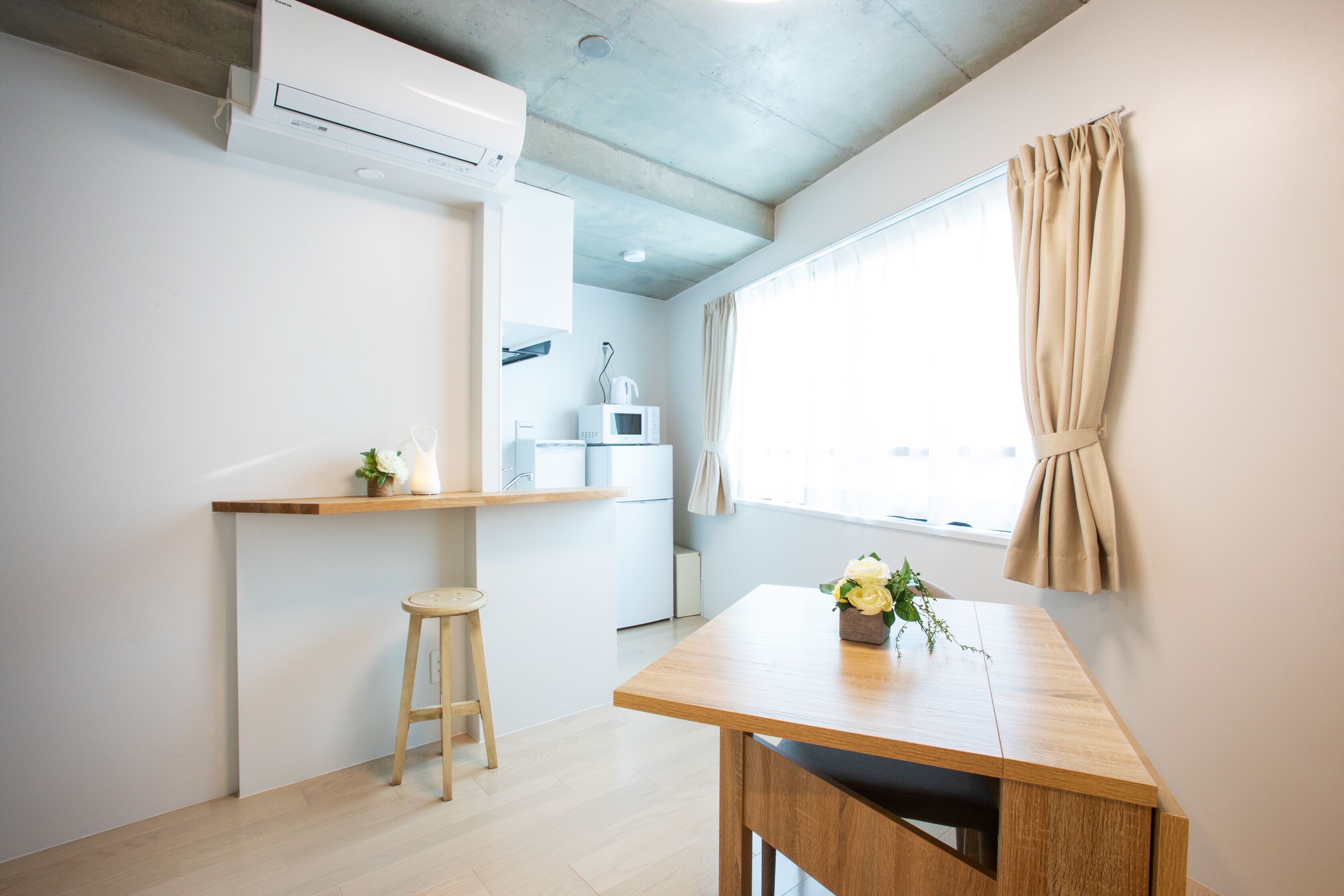 A modern kitchen with a wooden table, a stool, and a window with curtains.