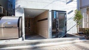A modern building entrance with a metal door, a small enclosed area with a bench, and a potted plant. - Laffitte Tokyo WEST (Tokyo)