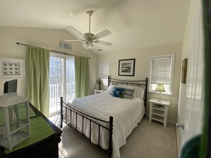 Une chambre à coucher comprenant un lit, un bureau, une chaise, un ventilateur de plafond et une fenêtre avec des rideaux.