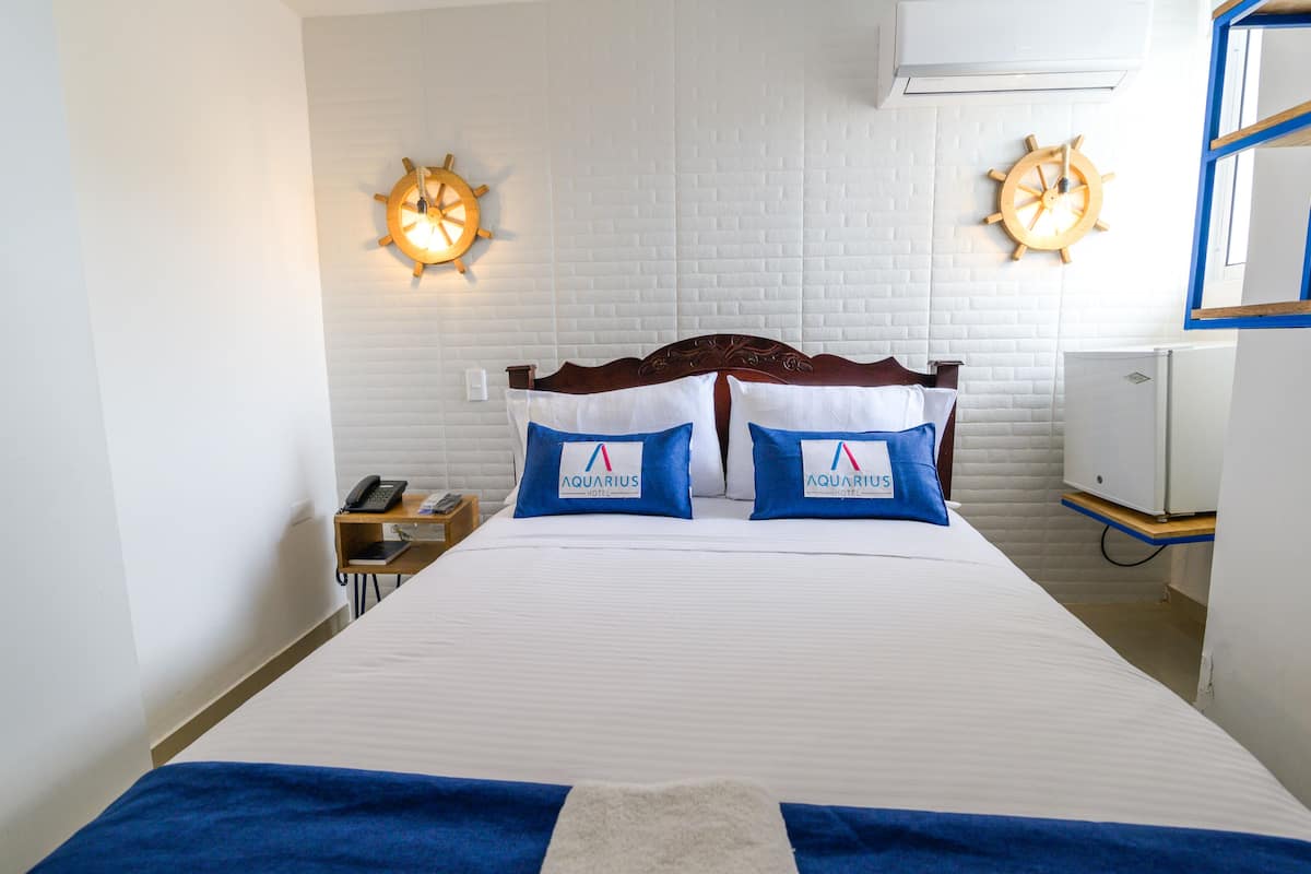 A hotel room with a large bed, two wall clocks, a desk with a phone, and a small white cabinet.