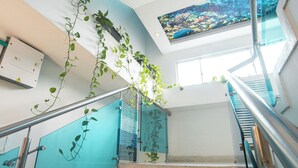 A staircase with glass railings, a ceiling mural, and a wall-mounted electrical box. - Hotel Aquarius (Barranquilla)