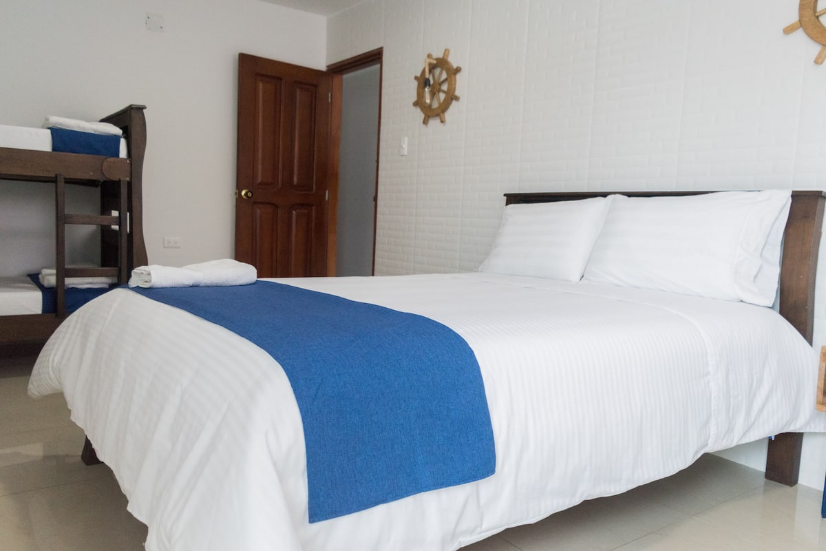 A neatly made bed with a blue blanket, a wooden headboard, and a wooden shelf with towels.