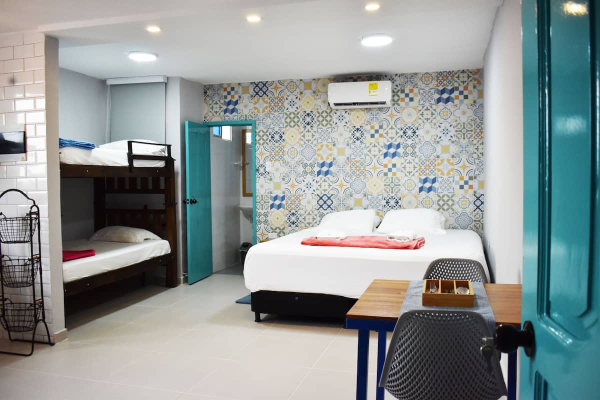 A room with a bunk bed, a single bed, a desk with a chair, and a tiled wall.