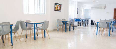 Un comedor amplio con varias mesas y sillas, ventanas grandes y ventiladores de techo.