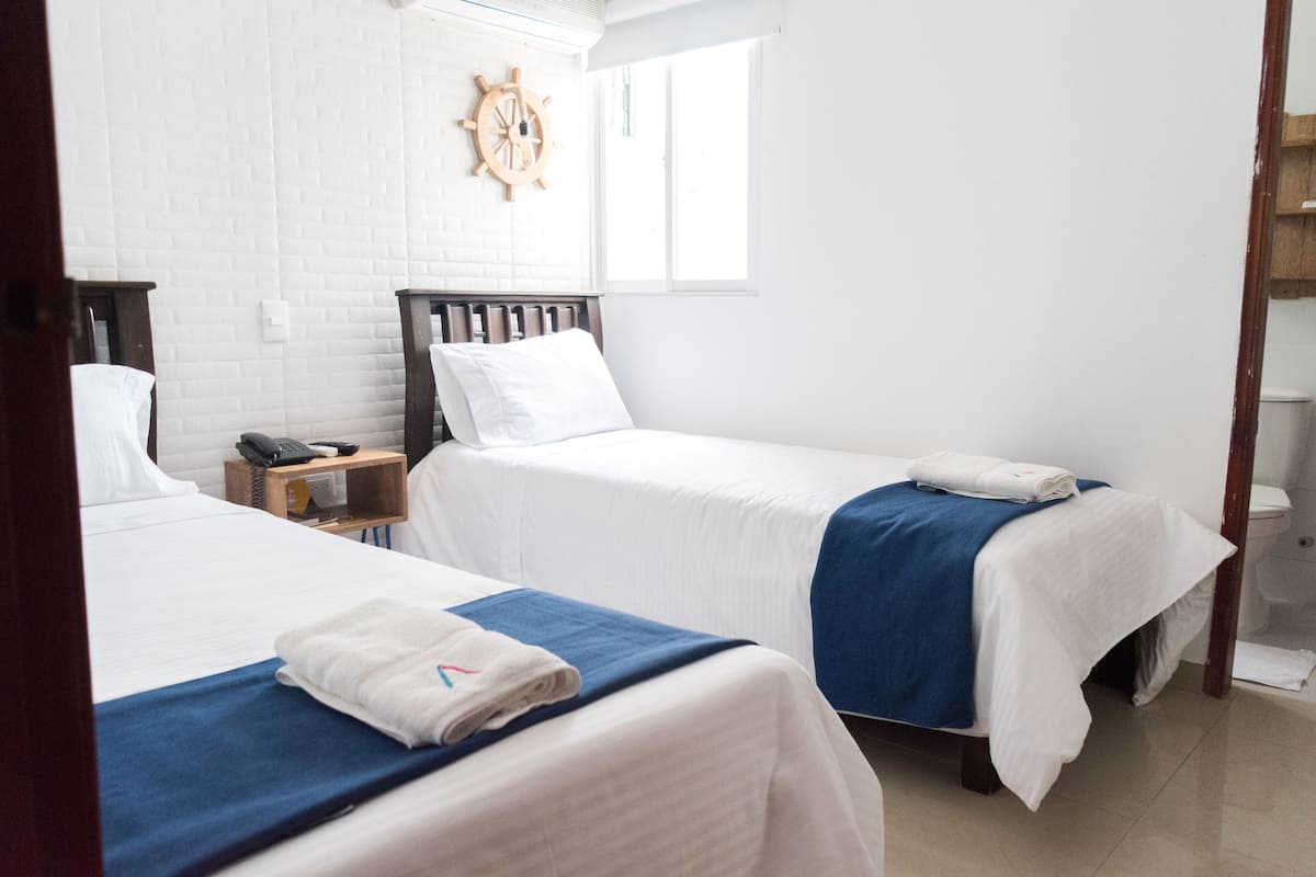A hotel room with two beds, white bedding, a wooden headboard, a wooden side table with a phone, and a ship's wheel on the wall.