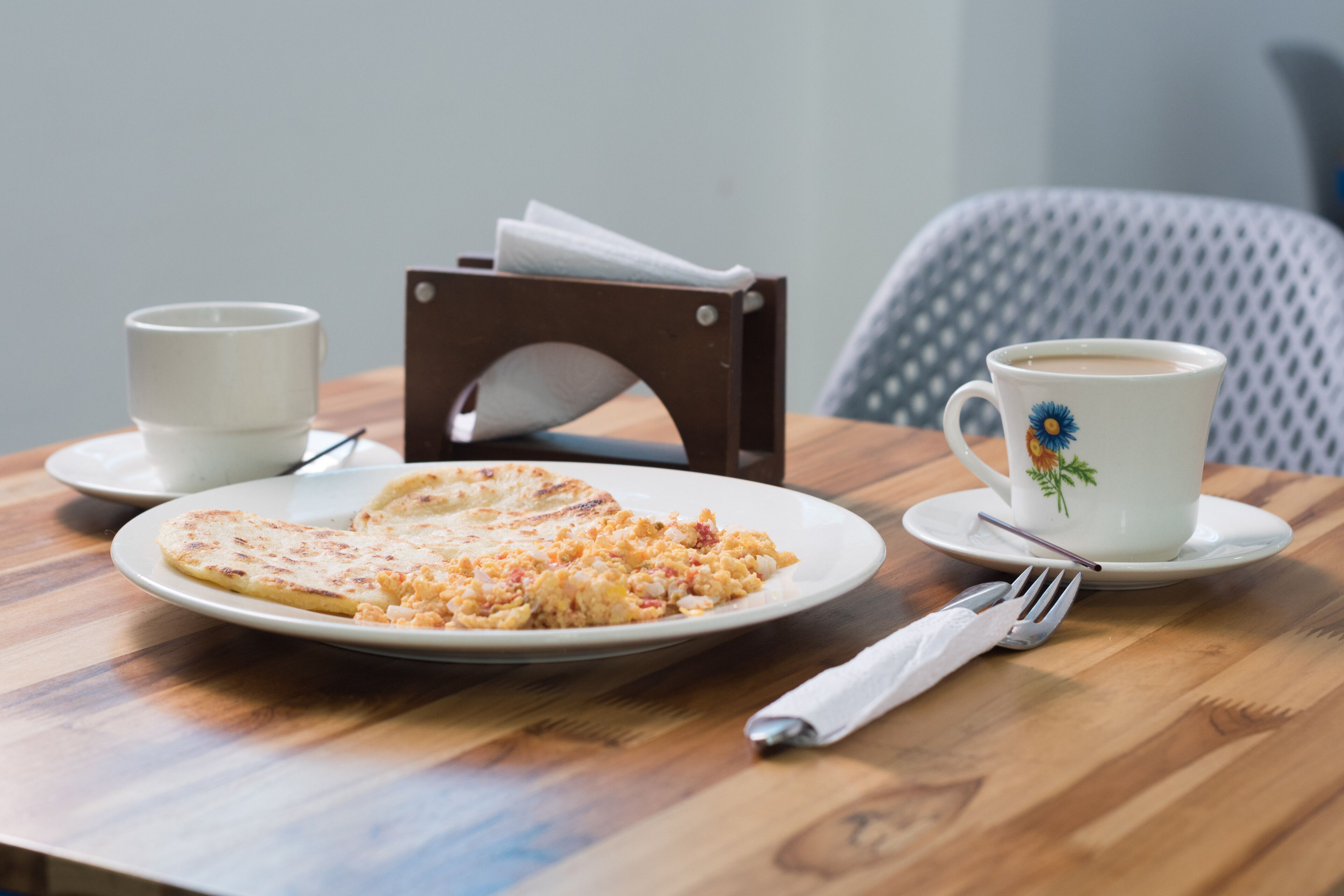 Una mesa de madera con un plato de comida, una taza de café y un portalápices.