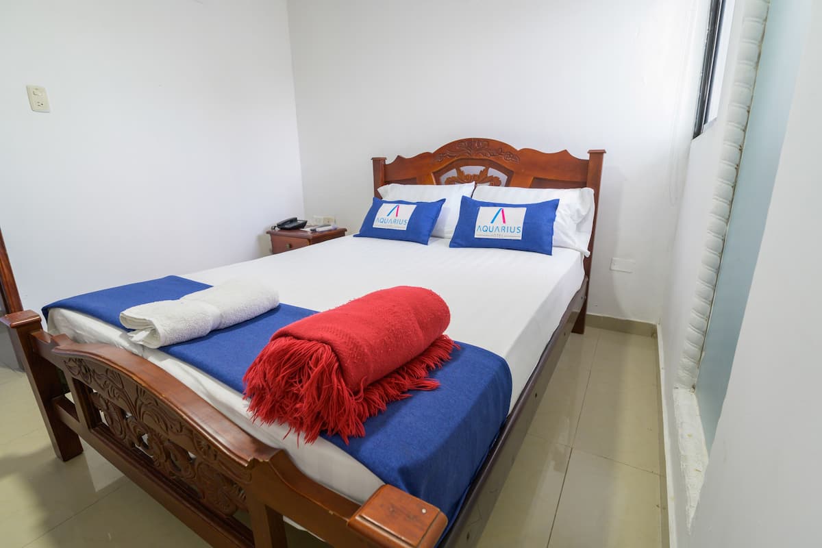 A neatly made bed with blue and white bedding, a red throw blanket, and two pillows with a logo.