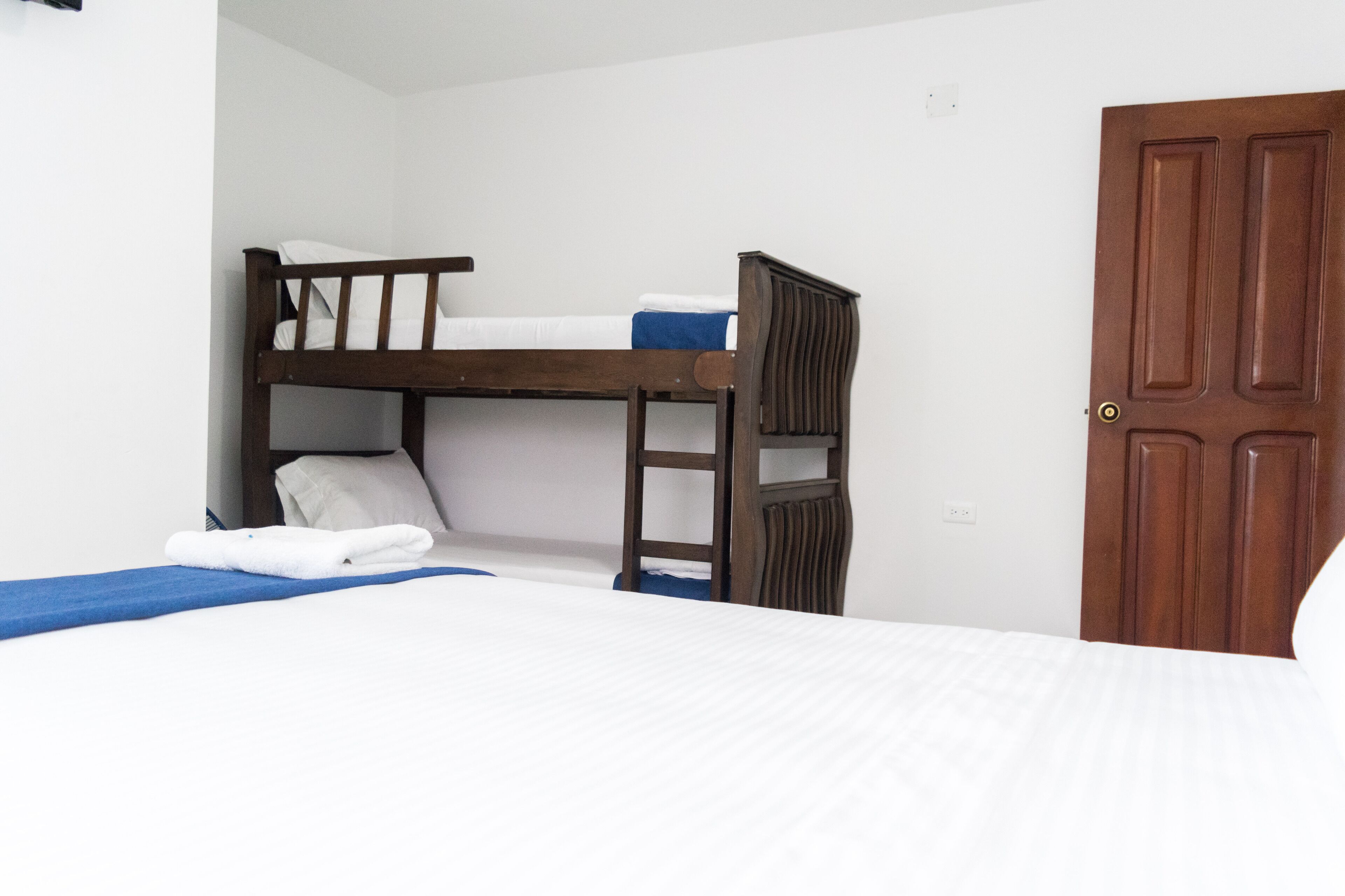 A bunk bed with white bedding and a blue blanket, a wooden door, and a white wall.