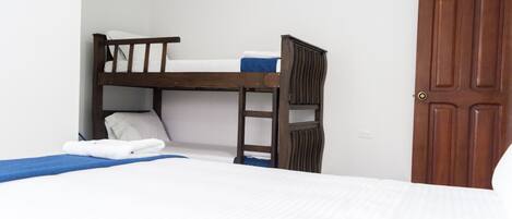 A bunk bed with white bedding and a blue blanket, a wooden door, and a white wall.