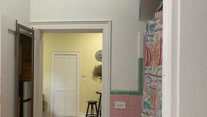 A narrow hallway with a tiled floor, a door leading to a room with a refrigerator, and a patterned rug. - MaryBo - Back Yard Oasis Studio (Nassau)