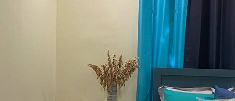 Une chambre à coucher avec un lit, une table de chevet, un vase contenant des plantes séchées, une télécommande et un climatiseur fixé au mur.