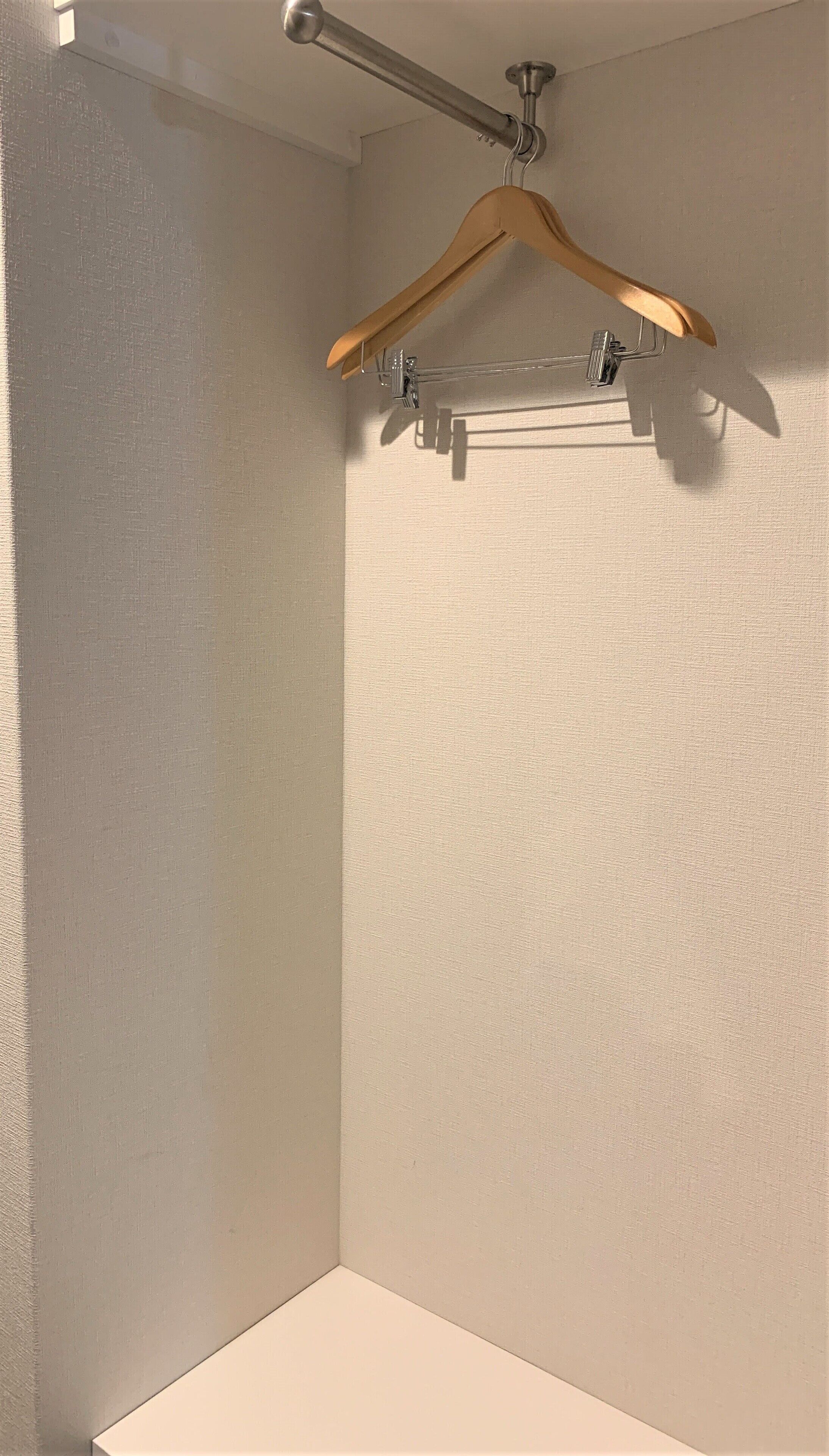 A corner of a room with a textured wall, a wooden hanger on a metal rack, and a ceiling-mounted rod.