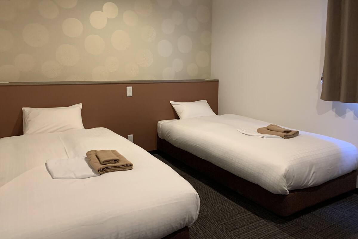 A hotel room with two beds, each with white linens and a brown headboard. There are folded towels on each bed.