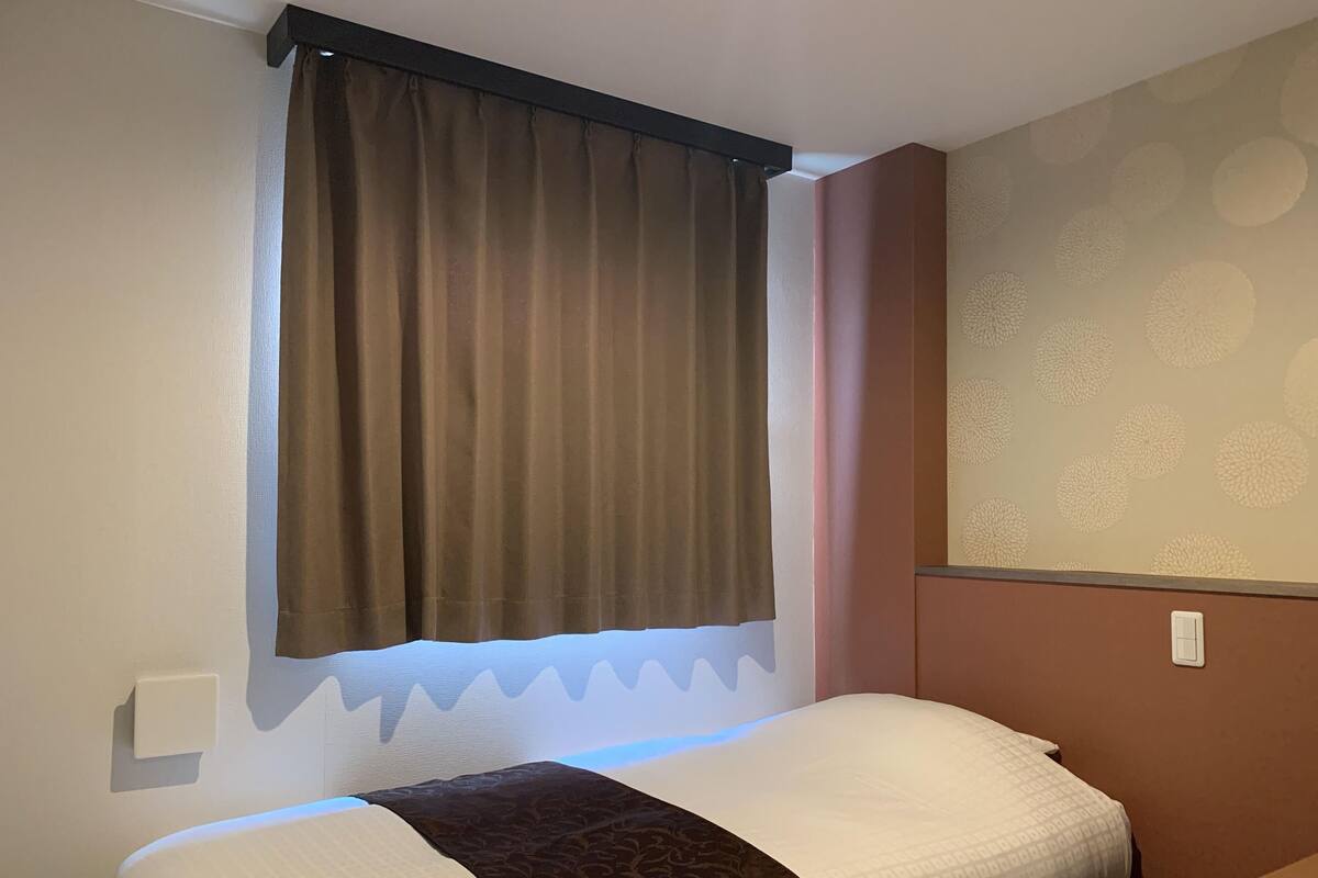 A hotel room with a bed, a window with curtains, a wall with a patterned design, and a light switch.