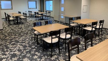 Un salón de conferencias con varias mesas y sillas, suelo alfombrado y ventanas con persianas.