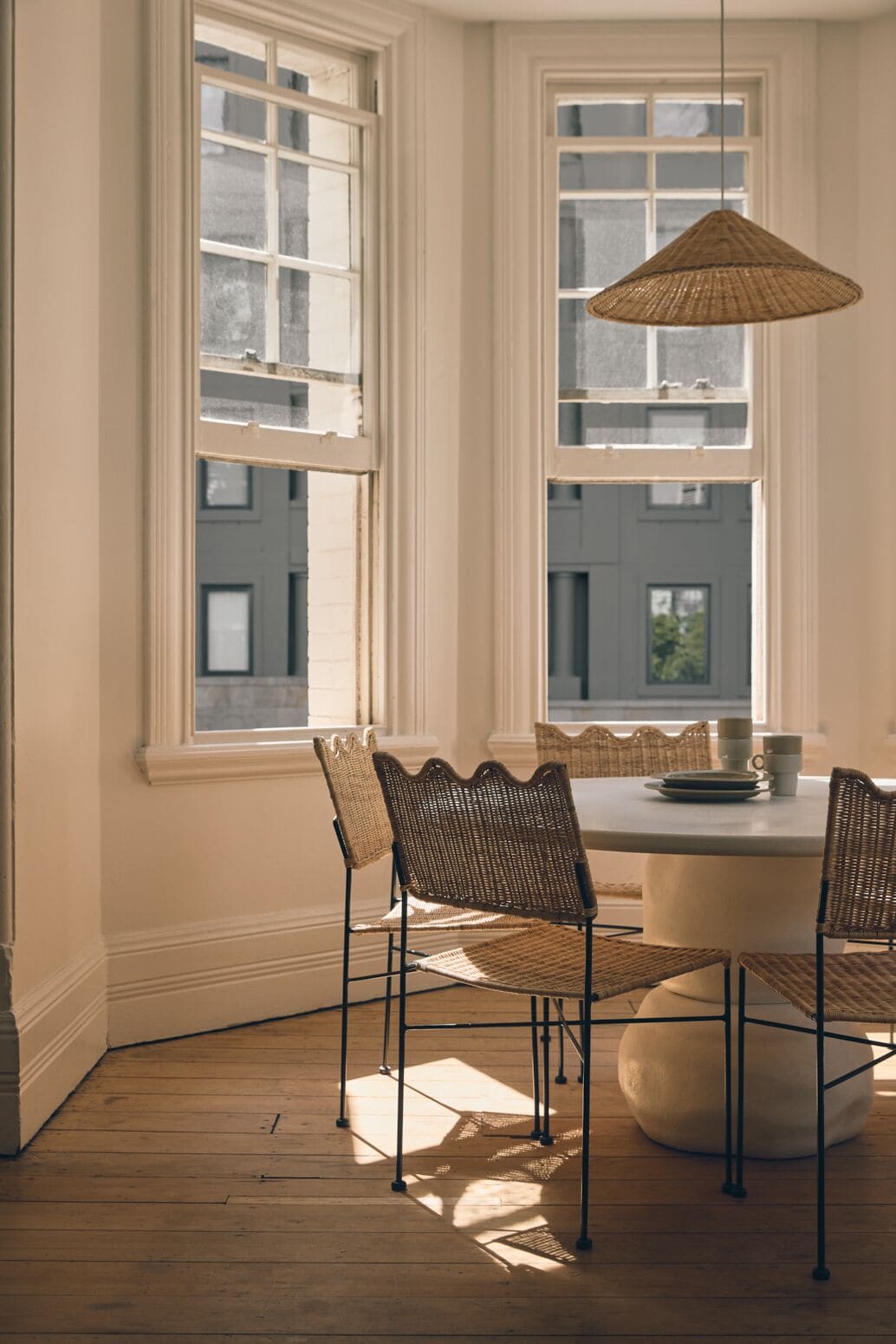 Un coin repas avec une table ronde, des chaises en osier et un luminaire suspendu.