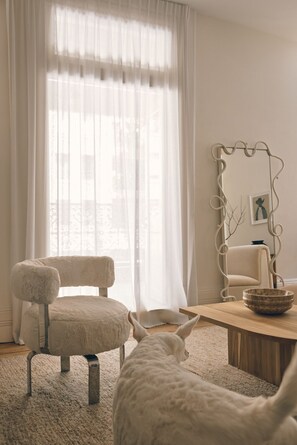 A room with a large window, a chair, a table with a bowl, and a decorative mirror. - Three Rooms Sydney (Potts Point)