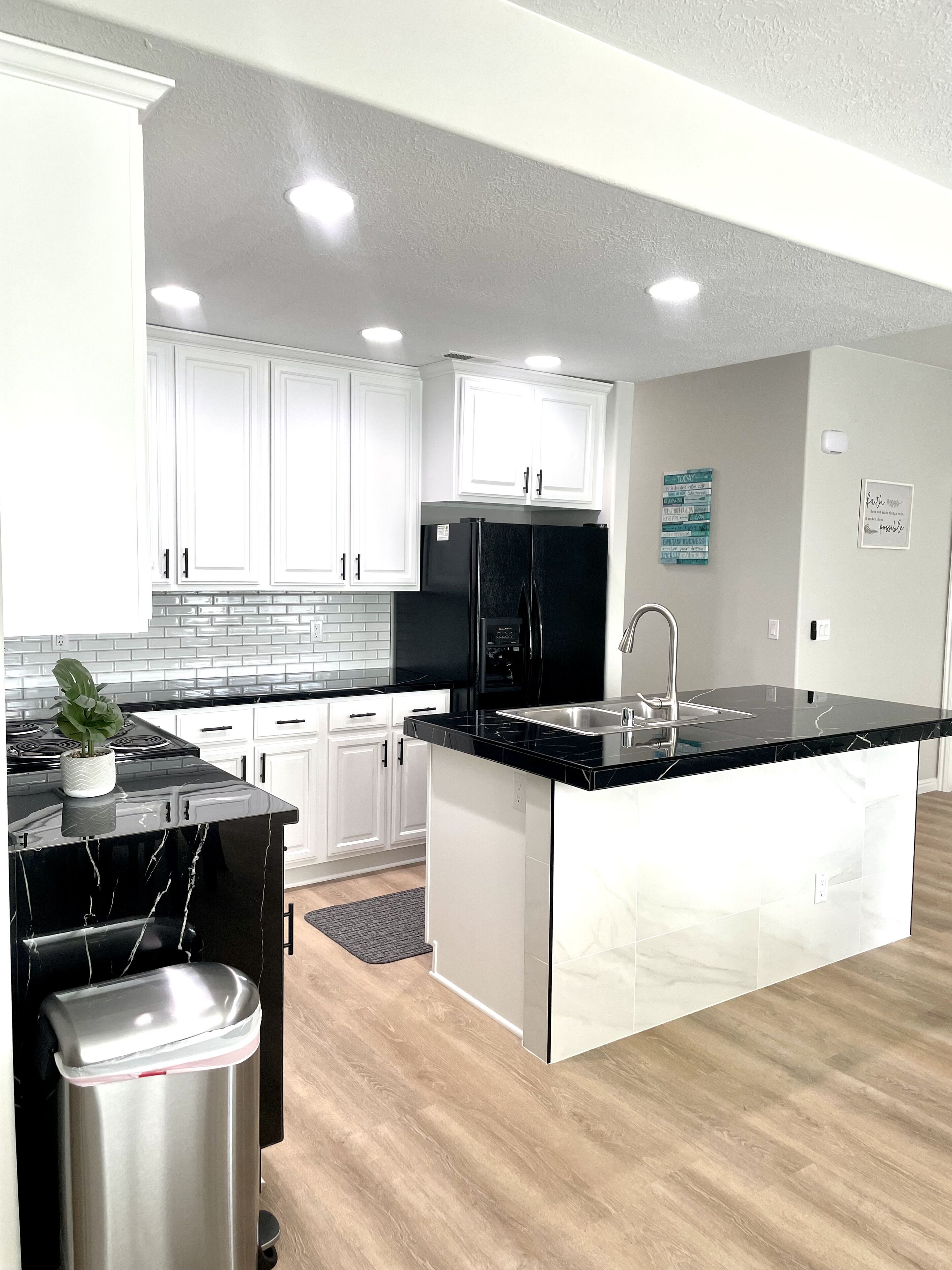 A modern kitchen with white cabinets, black appliances, and a marble countertop.