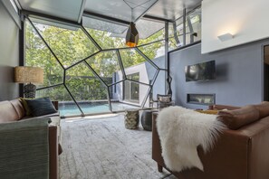Ein modernes Wohnzimmer mit Glasdecke, Blick auf einen Pool und einem braunen Ledersofa.