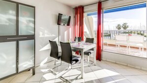 Una habitación moderna con una mesa de comedor, sillas, un televisor de pantalla plana y un balcón con cortinas rojas.